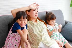 Asian single mom Headache raising two mischievous little children. The three of them sat on the sofa in the house. Family concept. Modern parenting, single mother, how to raise happy children. photo
