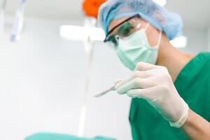 Asian professional surgeon holding a scalpel with glasses and wear gloves and a mask In the operating room in the hospital. Concept of medical services. cosmetic surgery. Copy space photo