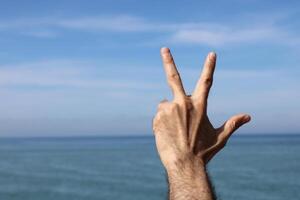 Hand doing,showing number three gesture symbol on blue summer sky nature background. Gesturing number 3. Number three in sign language. photo