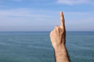 Hand doing,showing number gesture symbol one on blue summer sky nature background. Gesturing number 1. photo