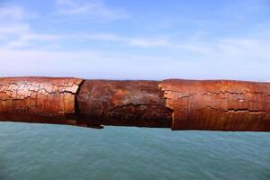 A rusty fence with a blue sea in the background.Rusty iron railing, beautiful sea and sky landscape view between rusty railing gap. photo