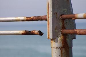 A rusty fence with a blue sea in the background.Rusty iron railing, beautiful sea and sky landscape view between rusty railing gap. photo