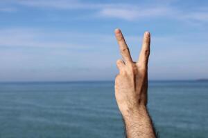 Hand doing,showing number two gesture symbol on blue summer sky nature background. Gesturing number 2. Number two in sign language. photo