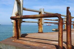 A rusty fence with a blue sea in the background.Rusty iron railing, beautiful sea and sky landscape view between rusty railing gap. photo