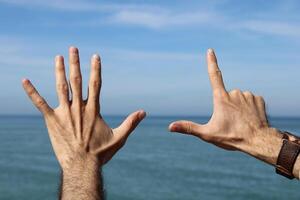 Hand doing,showing number gesture symbol seven on blue summer sky nature background. Gesturing number 7. Number seven in sign language. photo