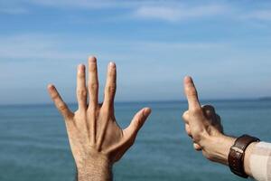 Hand doing,showing number gesture symbol six on blue summer sky nature background. Gesturing number 6. Number six in sign language. photo