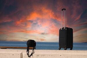 Suitcase and bag are standing on a beach with a sunset in the background.Travel and holiday concept photo