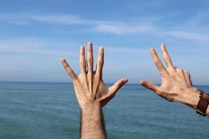 Hand doing,showing number gesture symbol eight on blue summer sky nature background. Gesturing number 8. Number eight in sign language. eighth. photo