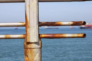 A rusty fence with a blue sea in the background.Rusty iron railing, beautiful sea and sky landscape view between rusty railing gap. photo