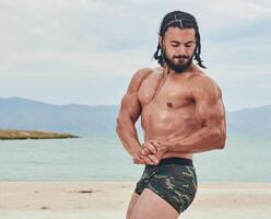 young muscular man exercising on the beach, young muscular man doing bodibuilding exercises on the beach, athletic young man on the beach photo