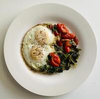 fried eggs with spinach and cherry tomatoes on a white plate, top view photo