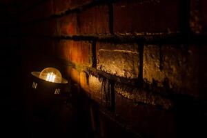 ligero en el oscuro, antiguo lámpara en el muro, antiguo ladrillo pared con ligero foto