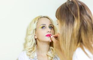 bonito joven mujer aplicando hacer arriba en belleza salón foto