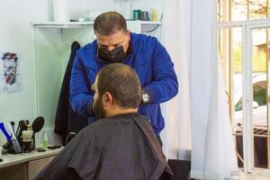 barber in medical mask cutting hair in barber shop, barber cutting hair photo