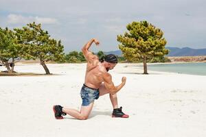 joven muscular hombre hacer ejercicio en el playa, joven muscular hombre haciendo culturismo ejercicios en el playa, atlético joven hombre en el playa foto