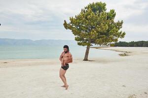 joven muscular hombre hacer ejercicio en el playa, joven muscular hombre haciendo culturismo ejercicios en el playa, atlético joven hombre en el playa foto