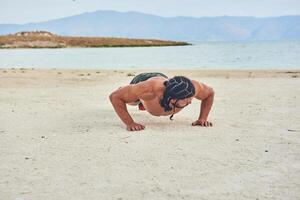 young muscular man exercising on the beach, young muscular man doing bodibuilding exercises on the beach, athletic young man on the beach photo