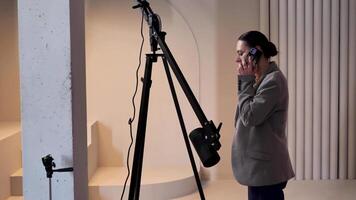 mujer, productor, fotógrafo en blanco foto estudio hablando en teléfono. conversacion con el cliente acerca de el coordinación de disparo y edición. medio plan, estático. video