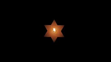 A lighted Jewish yellow candle in the shape of a star of David on Hanukkah. On a black isolated background close up in 4K without faces of people. video