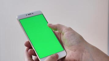 POV scrolling smartphone with green screen on white isolated background close-up in female hands. Modern technology, phone in real life video