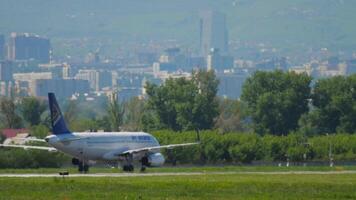 ALMATY, KAZAKHSTAN - MAY 5, 2019. Air Astana civil plane on the taxiway, haze. Airliner taxiing against the backdrop of a city in the mountains video