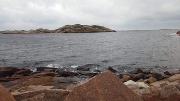 The strong wind creates small waves on the water on the rocks of the ocean coast in southwestern Sweden during autumn video