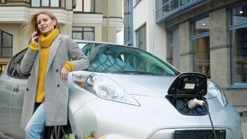 Woman talking on the phone while charging an electric car. Charging electric car at the electric gas station video