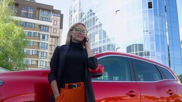 réussi femme d'affaires supporter près une rouge voiture tandis que parlant sur téléphone intelligent près affaires centre video