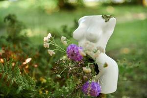 Female statue art object with flowers in stomach on outdoor green forest background photo