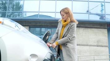 mujer enchufar en su eléctrico coche a cargar cerca negocio centrar video