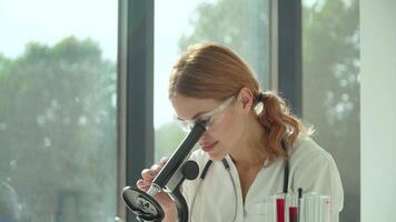 vrouw wetenschapper dokter aan het doen sommige Onderzoek en op zoek door een microscoop in laboratorium. bloed test video