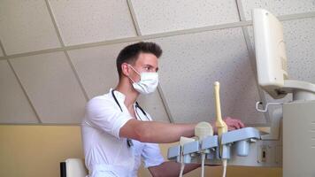 Breast cancer diagnosis. Young doctor in protective mask examines patient. Ultrasound devices monitor close-up. Possession of medical equipment video