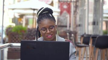 afrikanisch amerikanisch Frau im Straße Cafe funktioniert auf ihr Laptop. zurück beim Arbeit mit Sozial Entfernung Vorsichtsmaßnahmen video