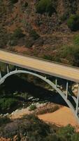 Bridge with cars moving by. Arched bridge in the mountains above the little creek. Aerial view. Vertical video