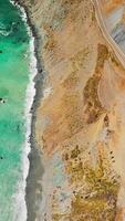 turkos hav vatten möte de klippig Strand av Kalifornien. topp se på de motorväg gående byggd på de berg. vertikal video