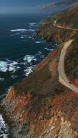 Magnificent mountains of California with highway in the middle. Dark blue ocean with white foamy waves. Aerial perspective. Vertical video