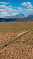 Two-lane road leading to the beautiful mountains. Highway to Nevada from California at backdrop of blue skies with fluffy clouds. Aerial view. Vertical video