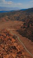 Highway passing among the craggy rocks and deserted landscape. Sunny day footage in the mountains of Nevada from aerial view. Vertical video