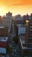 Rahmen Sonne Über das mehrstöckig Gebäude von Neu York. Drohne steigend Über ein beschäftigt Straße von Metropole. Orange Himmel Hintergrund. Vertikale Video