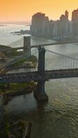 Manhattan and Brooklyn Bridges over East River. Silhouettes of New York skyscrapers at the backdrop of orange skies. Vertical video