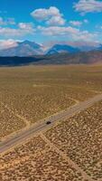 Motorway along the desert limited by mountain range. Soft cumulus clouds throwing shadows on the rocks. Aerial view. Vertical video