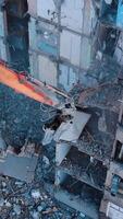 Excavator crashing floors of an old building and dusty debris falling down. Disassembling of collapsed structures. View from above. Vertical video