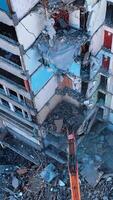 deconstructie van oud gebouwen met de graafmachine klauw. zwaar machinerie slopen puin en draaien het in stof. visie van bovenstaande. verticaal video