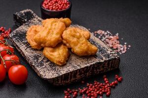 Delicious fresh crispy chicken nuggets on a dark concrete background photo