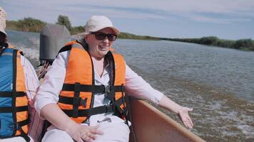 A happy female tourist touches the water from a boat while traveling on the river. A woman plays with water drops. Moments of tourism. Life is wonderful. Elderly tourism. video