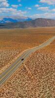 Lonely black car on the road to Nevada, USA. Beautiful sight of desert contrasting with blue skies. Mountains at backdrop. Vertical video