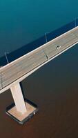 Approaching and flying over the bridge connecting Martinez to Benicia. Cars moving by the bridge in same direction. Top view. Vertical video