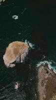 Desolate rocks peeping out from aquamarine water of Pacific at the coast of California. Some algae clusters floating on the water. Top view. Vertical video