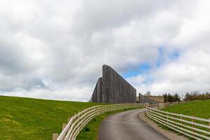 Curved road leading to a modern wooden building with a unique design, under a cloudy sky. photo