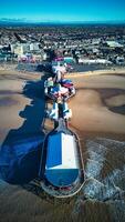 Aerial view of a vibrant pier with amusement rides extending into the sea, with a sandy beach and cityscape in the background in Backpool, England. photo